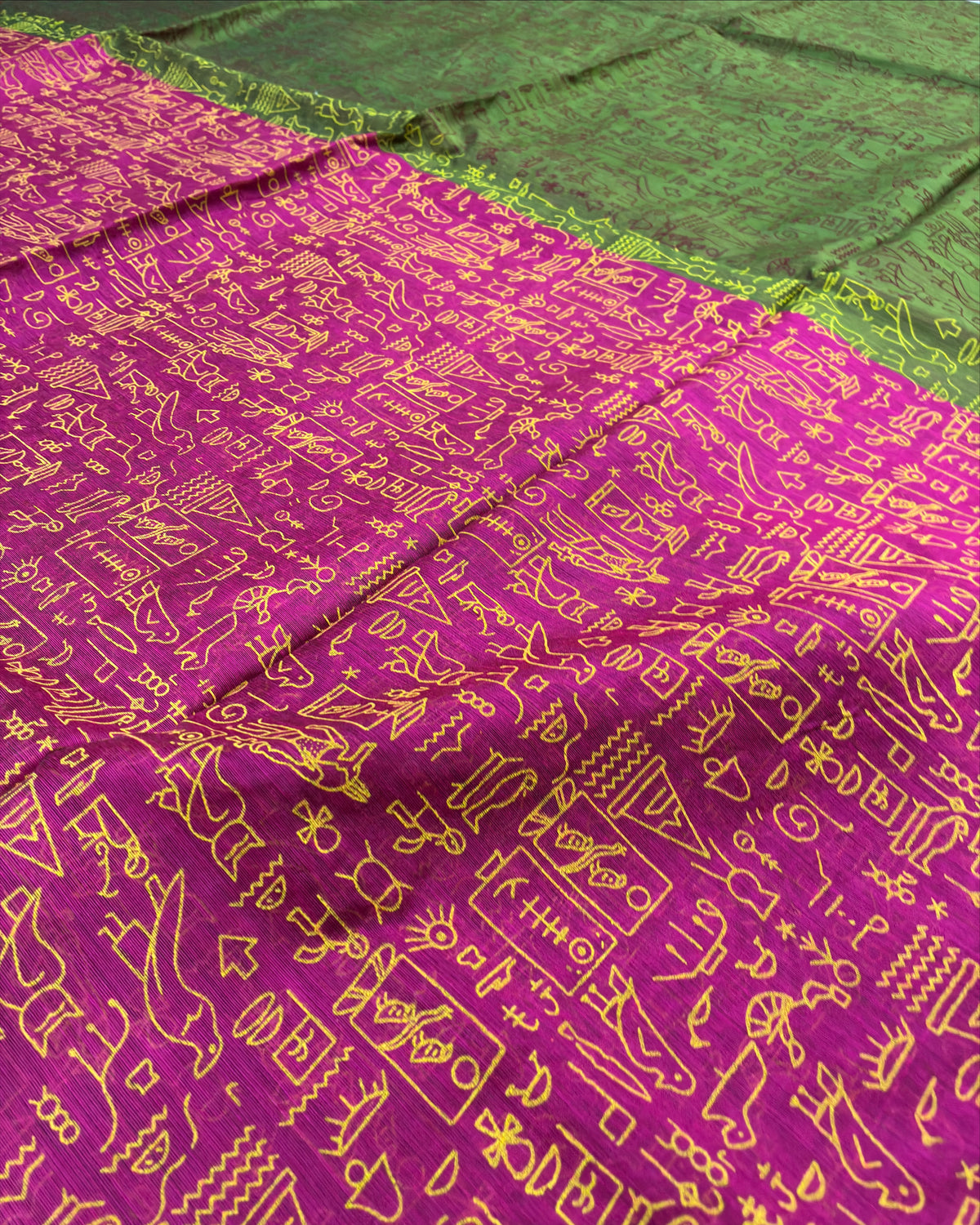 A close-up of a magenta purple fabric with yellow printed patterns, laid next to a green fabric with yellow fringe.