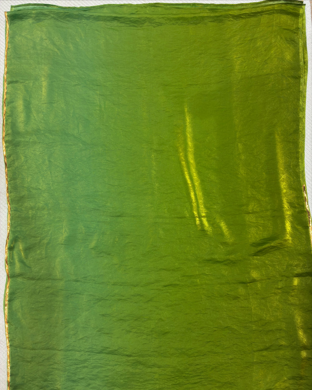 A square green fabric or material sample with a slightly crinkled texture and subtle sheen, shown flat against a light background.