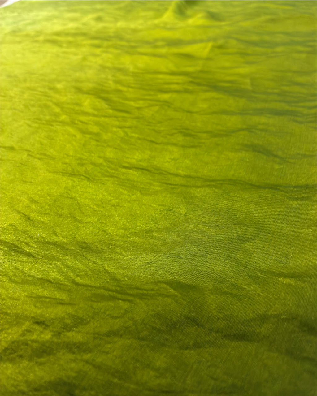 A close-up of crinkled olive green fabric filling the frame, showing a textured material surface with subtle sheen and folds.