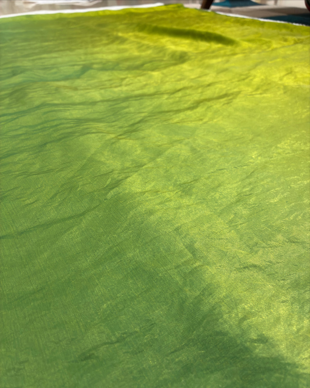 A close-up of a bright lime green textured fabric, likely a tablecloth or patio cover, draped outdoors with natural light casting soft shadows across its surface.